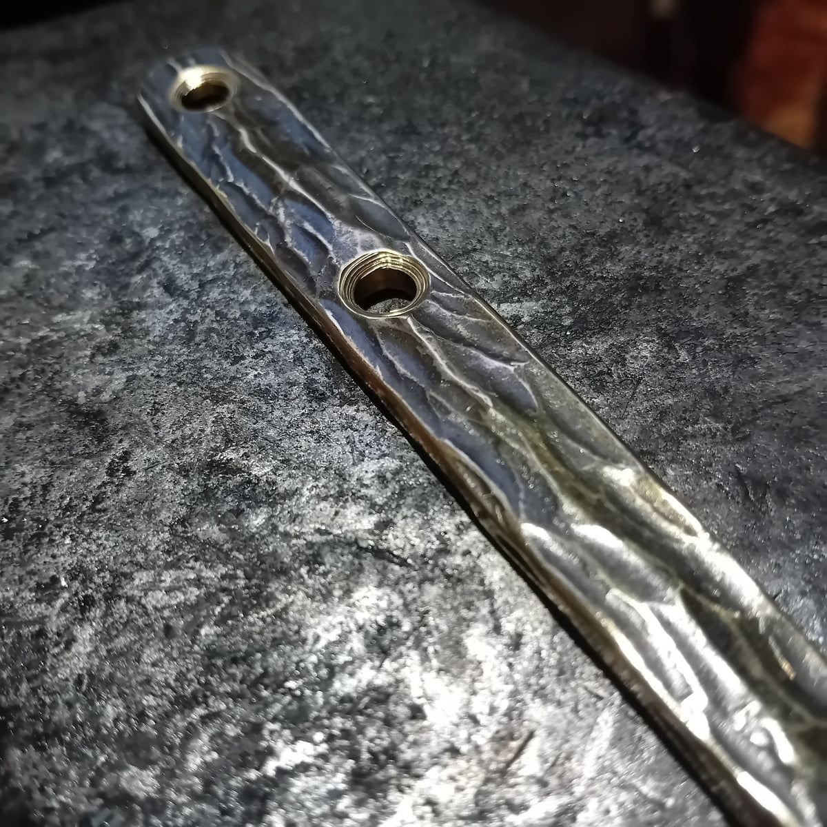 Detail of countersunk fixing holes in a hand-forged brass wall hook