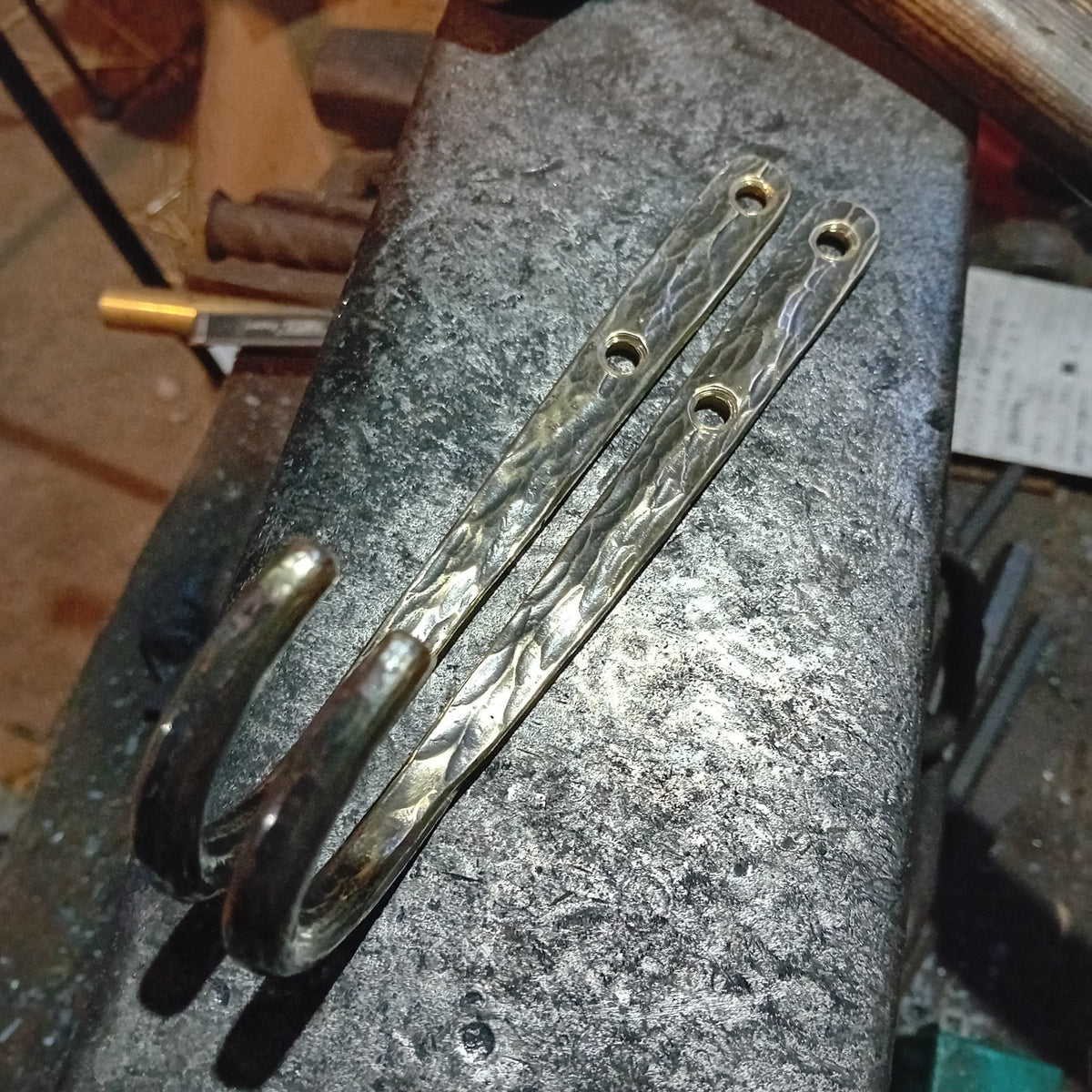 Two large brass wall hooks showing their curved ends and double fixing holes