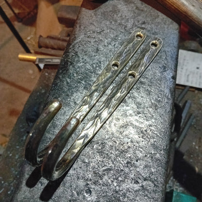 Two large brass wall hooks showing their curved ends and double fixing holes
