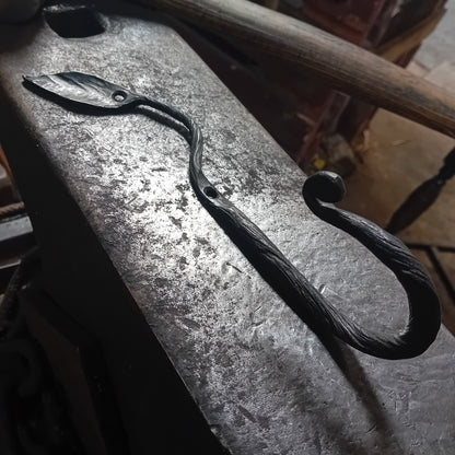 Hand-forged botanical leaf wall hook with twisted stem and scroll end on blacksmith anvil