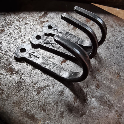 Close-up of three small hand-forged rune hooks showing fixing holes and curved hooks