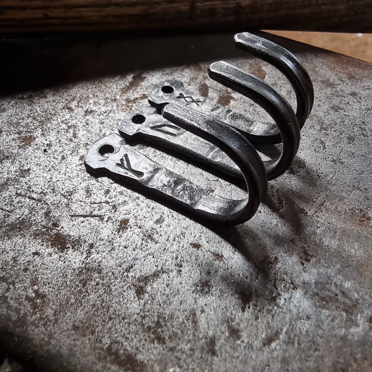 Three hand-forged steel rune hooks on a textured metal surface, showing individual rune engravings