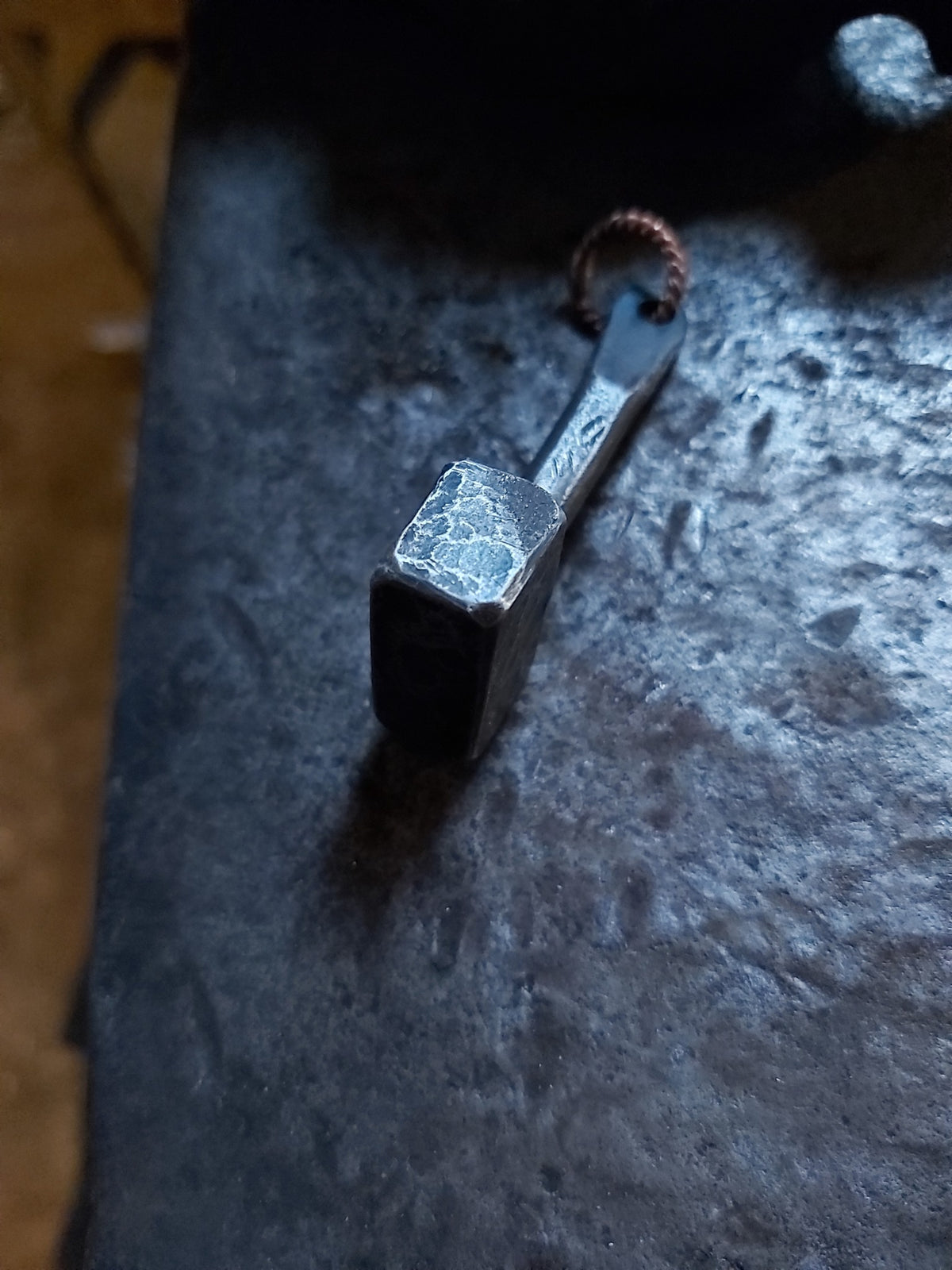 Side view of hand-forged steel Thor's hammer pendant on an anvil