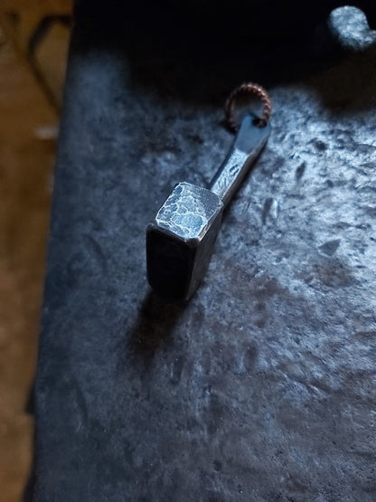 Side view of hand-forged steel Thor's hammer pendant on an anvil
