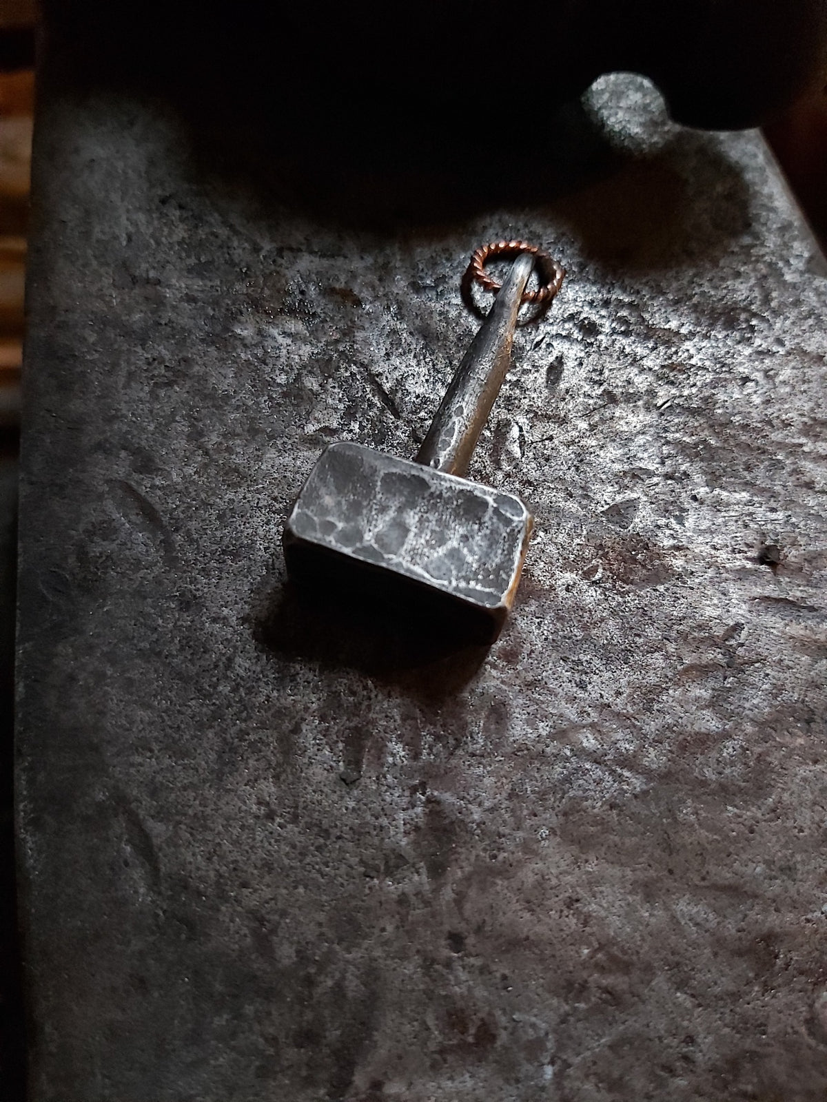 Hand-forged Mjolnir steel pendant showing textured hammer face and copper loop