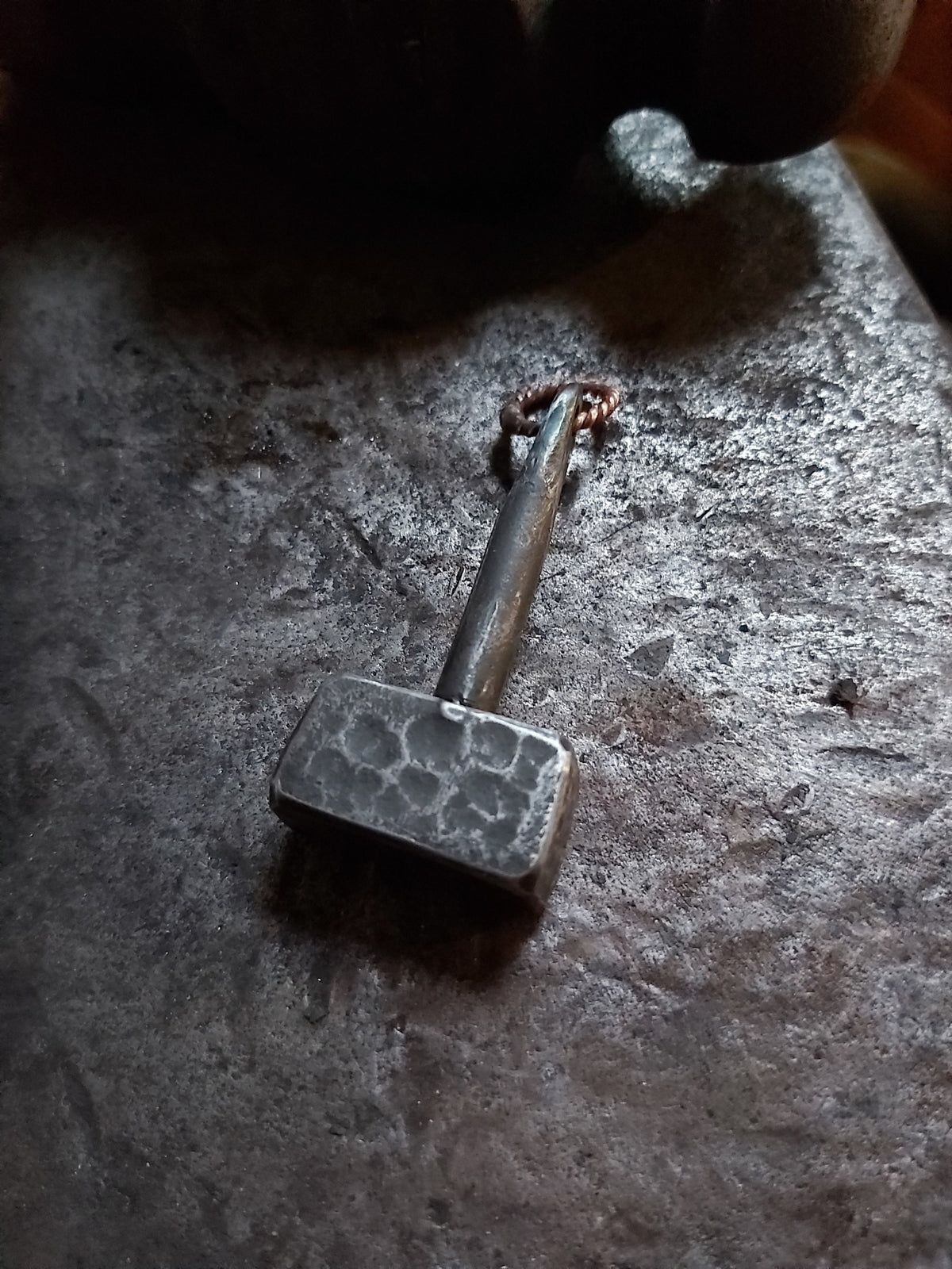Close-up of handmade Thor's hammer pendant on a forge anvil